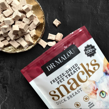 Dr Malou liofilizowane przysmaki z kaczki dla kota, opakowanie i kostki w złotej misce na ciemnym tle.