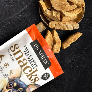 Dr Malou liofilizowane kostki łososia, otwarta biało-pomarańczowa torba i rozsypane chrupki na ciemnym blacie.