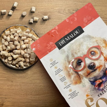 Opakowanie Dr Malou liofilizowanej karmy dla psa Kaczka z królikiem i kawałki jedzenia na drewnianym blacie.