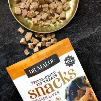 Biało-pomarańczowe opakowanie Dr Malou: liofilizowana wątroba kurczaka dla psów i kotów. Rozsypane brązowe kostki.