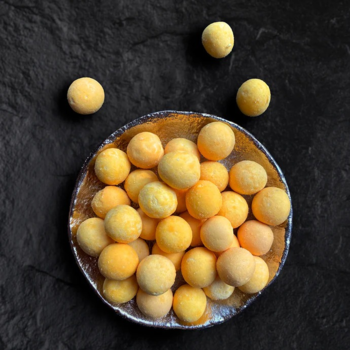 Liofilizowane żółtko przepiórcze Dr Malou dla kota, żółte, okrągłe przysmaki w dekoracyjnej misce na ciemnym blacie.