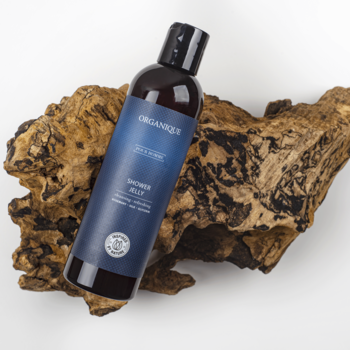 Organique Shower Jelly Pour Homme, brązowa butelka z granatową etykietą, leżąca na tle naturalnego drewna.