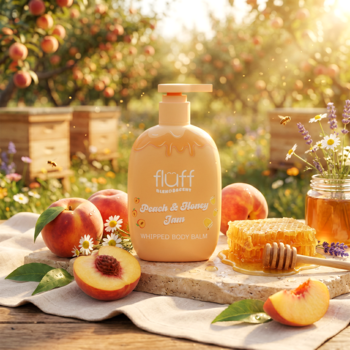 Balsam Fluff Peach & Honey Jam w brzoskwiniowej butelce, otoczony świeżymi brzoskwiniami i plastrem miodu.