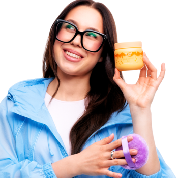 Kobieta w okularach prezentuje puder Fluff Peach Honey Jam w żółtym słoiku i fioletową szczotkę.