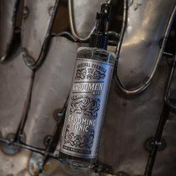 Groomen WIND Grooming Tonic, szklana butelka z atomizerem, srebrna etykieta, widok na industrialnym tle.