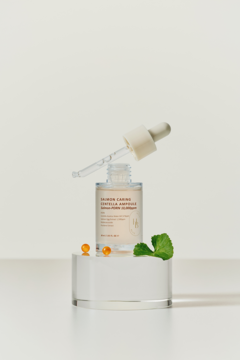 Serum do twarzy Round Lab z sokiem brzozowym w butelce z pipetą na białym bloku, obok granulki i mięta.