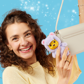 Kobieta prezentuje fioletowy pluszowy brelok Disney YuYus Kubuś Puchatek z winylową buzią, na tle torebki.