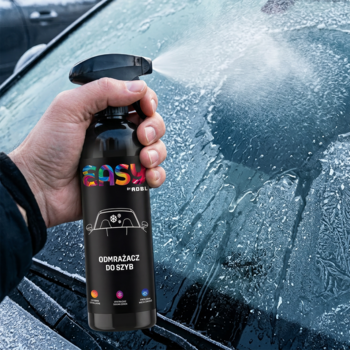 Dłoń aplikująca czarny odmrażacz do szyb Easy w sprayu na pokrytą szronem przednią szybę samochodu.
