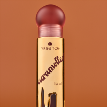 Złoty olejek do ust Essence Caramelted 01. Butelka z karmelowymi kroplami, czerwonawą nakrętką, pionowe ujęcie.