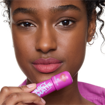 Kobieta z matową pomadką essence JUICY MATTE na ustach, trzymająca różową tubkę produktu.