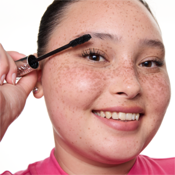 Uśmiechnięta kobieta nakłada czarną maskarę essence Lash PRINCESS volume & length PARTY na rzęsy. Bliskie ujęcie.
