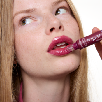 Zbliżenie na kobietę, która aplikuje lśniący balsam do ust essence super peptide 08 Cherrylicious. Usta błyszczą wiśniowym kolorem.