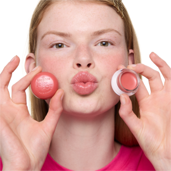 Kobieta z dzióbkiem trzyma słoiczki balsamu essence jelly POT 10 Hug Me! do ust/policzków. Różowy, otwarty i zamknięty.