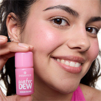 Zbliżenie na uśmiechniętą kobietę trzymającą różowy essence water DEW serum blush; na policzkach ma świeży róż.