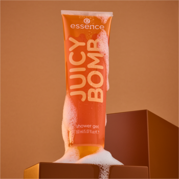 Pomarańczowa tubka żelu pod prysznic essence JUICY BOMB Caramel Splash, z obfitą pianą, na tle w odcieniach brązu.