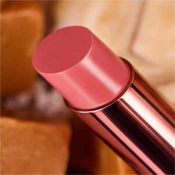 Zbliżenie lśniącego błyszczyka essence caramelted w sztyfcie w kolorze różanego różu, w różowo-złotym opakowaniu, na karmelowym tle.