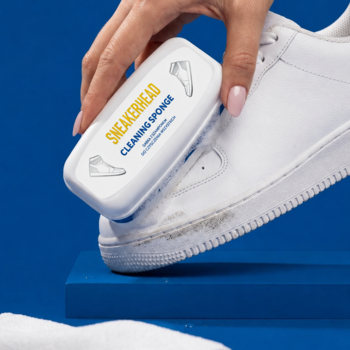 Biała gąbka SNEAKERHEAD czyści zabrudzonego białego sneakera. Widok z bliska na proces czyszczenia.