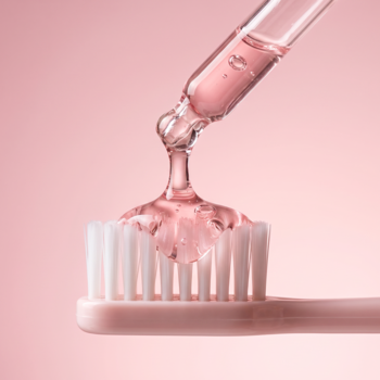 UltraBlanc Serum, różowy żel nakładany pipetą na różową szczoteczkę do zębów na jasnoróżowym tle. Pielęgnacja jamy ustnej.