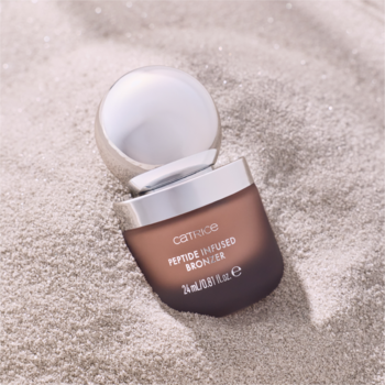 Bronzer Catrice SEASHELL STORIES z peptydami w ciemnej buteleczce ze srebrną zakrętką, na piasku. Ciepły brąz.