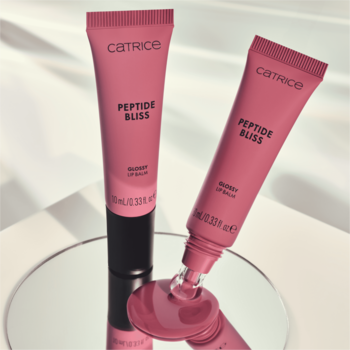 Dwa tubki Catrice Peptide Bliss Glossy Lip Balm w odcieniu jagodowym na lustrze, jeden z wyciśniętym błyszczykiem.