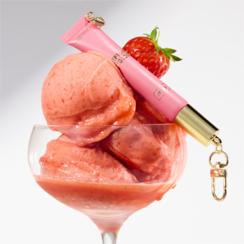Różowy błyszczyk Catrice THE SUMMER EDIT C01 Strawberry Sorbet z zawieszką, na truskawkowym sorbecie w kieliszku.