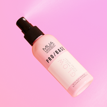Różowa mgiełka MUA PRO/BASE Glow Mist z czarnym atomizerem, rozpylająca drobny strumień na różowym tle.