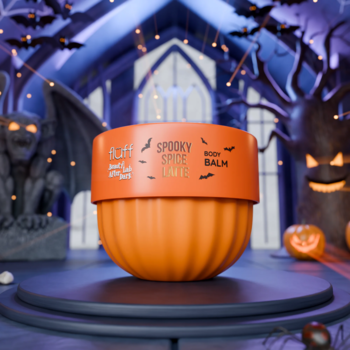 Pomarańczowy balsam do ciała Fluff Spooky Spice Latte w kształcie dyni na platformie, halloweenowe tło.