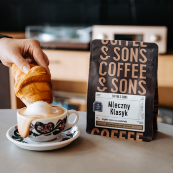 Opakowanie kawy ziarnistej Coffee & Sons Mleczny Klasyk 100% arabica. Ręka macza croissant w białej filiżance latte.