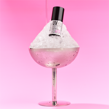 Czarna butelka matowego topu do paznokci essence UV GEL NAIL Frosted Scoop 01, w srebrnym kieliszku z lodem na różowym tle.