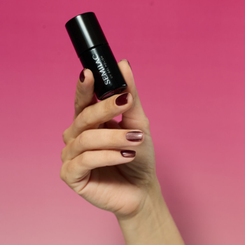 Dłoń trzyma czarny lakier Semilac 965 Chocolate Gloss. Paznokcie pomalowane na brązowo z magnetycznym efektem gloss.