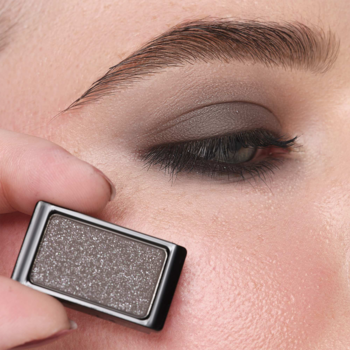 Zbliżenie na oko z brokatowym cieniem Artdeco Glam Smokey Black. Dłoń trzyma pojedynczą paletkę cienia.