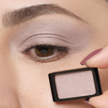 Kobieta z perłowo-satynowym cieniem Artdeco Pearly Smokey Lilac na powiece, trzyma wkład, zbliżenie.