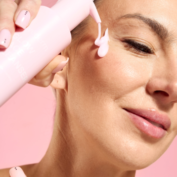 Kobieta nakłada różowy żel Swederm Glow Face Cleanser na policzek z butelki z pompką, zbliżenie.