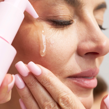 Zbliżenie na kobietę aplikującą olejek do demakijażu Oil Face Cleanser na policzek, różowa butelka.