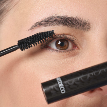 Zbliżenie: kobieta aplikuje Art Couture Lash Volumizer, czarny tusz do rzęs, który nadaje objętość i długość.