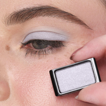 Zbliżenie na oko z brokatowym cieniem Artdeco Glam Light Blue; palec trzyma mały wkład cienia obok.