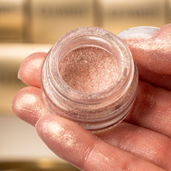 Zbliżenie na sypki pigment Glamtes Rosy Embrace w słoiczku, pudrowo-różowy z satynowym blaskiem, w dłoni.