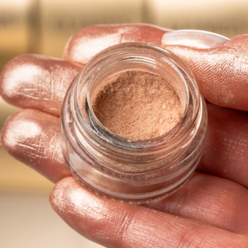 GLAMTES Golden Shimmer 06, sypki pigment złoto-szampański w małym, otwartym słoiczku trzymanym w dłoni.