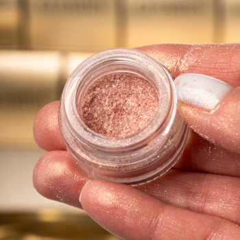 Zbliżenie: różowy perłowy pigment do makijażu Glamtes Pink Velvet w otwartym słoiczku trzymanym w dłoni.