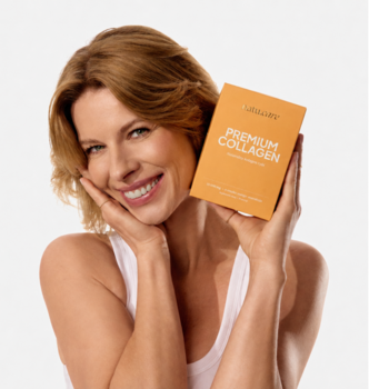 Uśmiechnięta kobieta z rudoblond włosami trzyma pomarańczowy kartonik Premium Collagen dla urody.