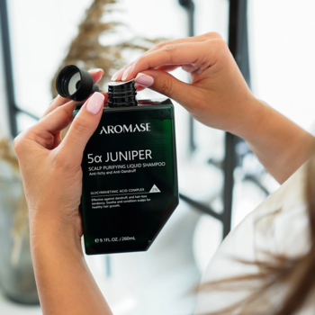 Dłonie otwierają ciemnozielony szampon Aromase 5a Juniper Scalp Purifying Liquid Shampoo, widoczny dozownik.