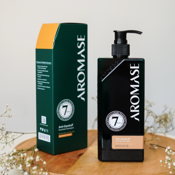 Aromase Anti-Dandruff Essential Shampoo, czarna butelka z pompką i zielono-pomarańczowe pudełko, na drewnie.