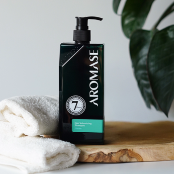 Aromase Hair Volumizing Shampoo, ciemnozielona butelka z pompką, na drewnie, obok biały ręcznik, przód-bok.