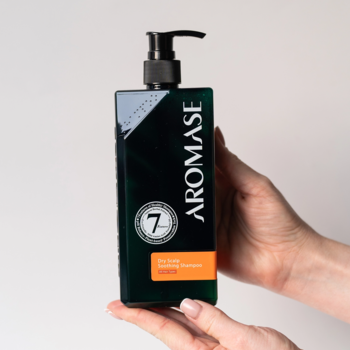 Aromase Dry Scalp Soothing Shampoo w ciemnej, prostokątnej butelce z pompką, trzymany w dłoniach, z widocznym napisem AROMASE.