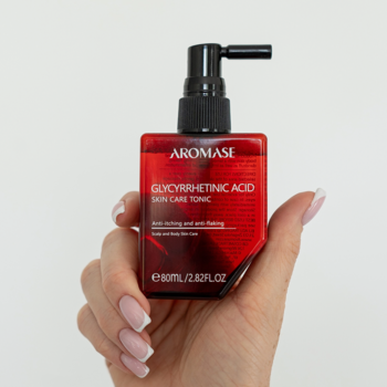Czerwony tonik AROMASE Glycyrrhetinic Acid na swędzącą skórę głowy, w kwadratowej butelce z pompką, trzymany w dłoni.