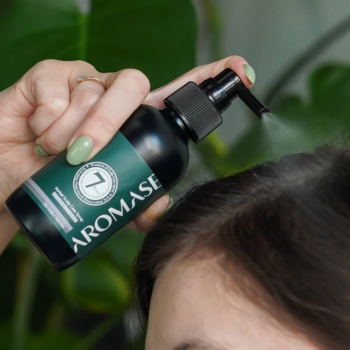 Dłoń aplikuje ziołowy spray AROMASE Herbal Scalp Care na skórę głowy, butelka 7 z zieloną etykietą.