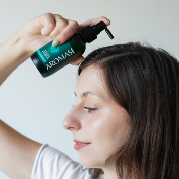 Kobieta aplikuje ziołowo-chłodzącą wcierkę AROMASE z pompką na przetłuszczającą się skórę głowy.