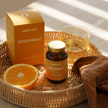 Pomarańczowe pudełko i brązowa butelka Natu.Care Witamina C PureWay-C® na tacy, z pomarańczą i szklanką napoju.