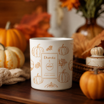 Świeca Durola Pumpkin Spice w białym słoju z dyniowym wzorem, na tle jesiennych liści i prawdziwych dyń.