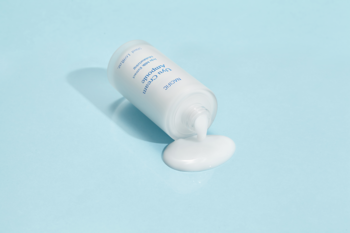 Biała butelka nawilżającej ampułki Nacific Uyu Cream Ampoule, leżąca na błękitnym tle, z wylaną kremową treścią.
